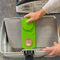 Bright green reusable filter bag with red circular opening attached to a Festool Midi dust extractor, held in hands over the white collection box