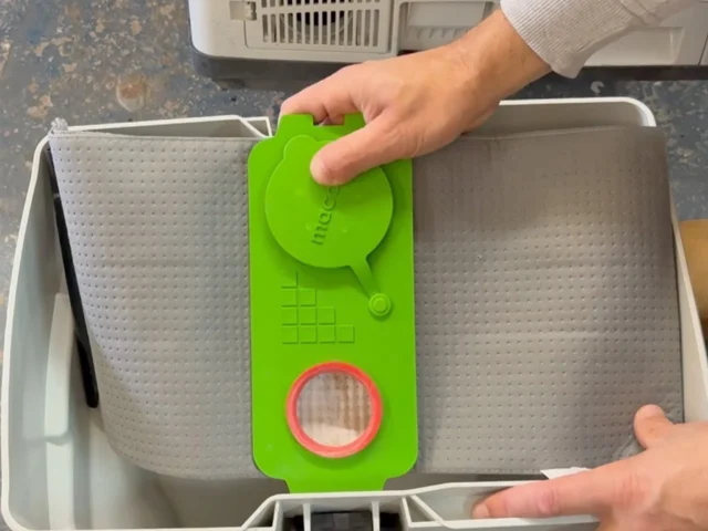 Bright green reusable filter bag with red circular opening attached to a Festool Midi dust extractor, held in hands over the white collection box