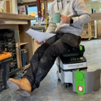 Green and white reusable filter bag with red button shown next to a Festool Midi dust extractor in a workshop
