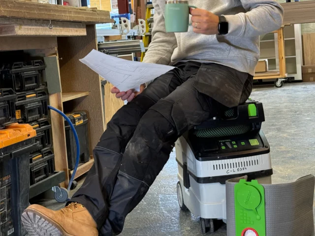 Green and white reusable filter bag with red button shown next to a Festool Midi dust extractor in a workshop