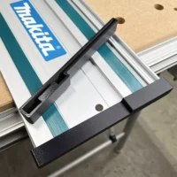 Black PETG protective caps attached to both ends of a Makita guide rail mounted on a track saw over a wooden workpiece