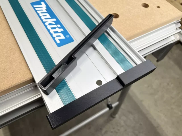 Black PETG protective caps attached to both ends of a Makita guide rail mounted on a track saw over a wooden workpiece
