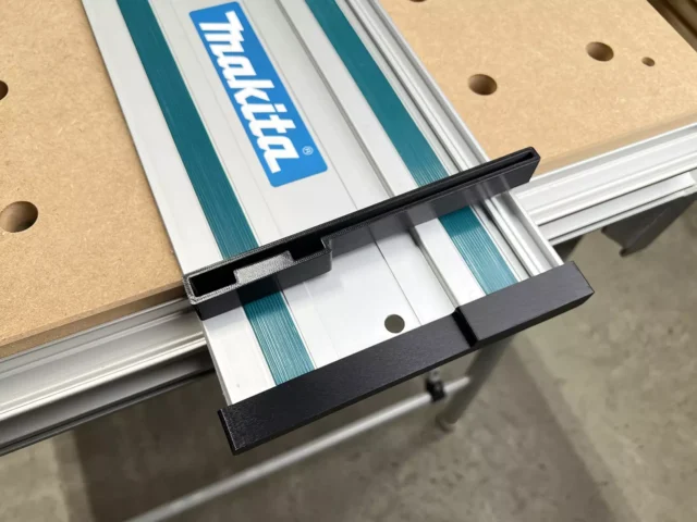 Black protective caps attached to each end of a Makita guide rail mounted on a track saw, with friction-fit design visible