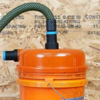 Two black 27mm hose adapters with blue bands on an orange Dustopper cyclone lid, one joined to a braided hose