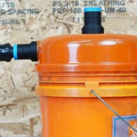 Two black ToolCurve 1-1/4 inch hose adapters with blue rings fitted to a Dustopper cyclone separator on an orange bucket, one joined to a hose