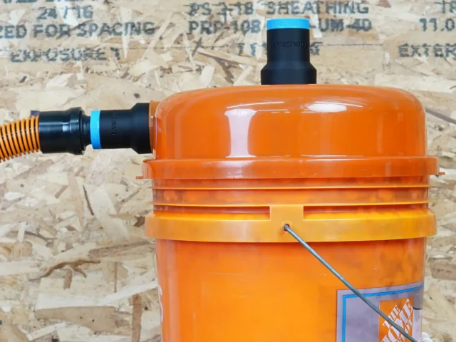 Two black ToolCurve 1-1/4 inch hose adapters with blue rings fitted to a Dustopper cyclone separator on an orange bucket, one joined to a hose