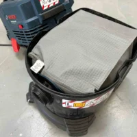 Gray reusable dust bag installed in black Bosch VAC090 9 gallon dust extractor, shown from above with Bosch power tool visible in background