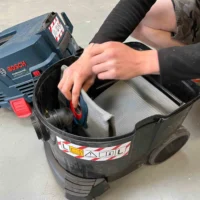 Macam reusable dust bag installed in Bosch VAC090 9-gallon dust extractor, showing gray three-layer polyester fleece material inside black collection basket