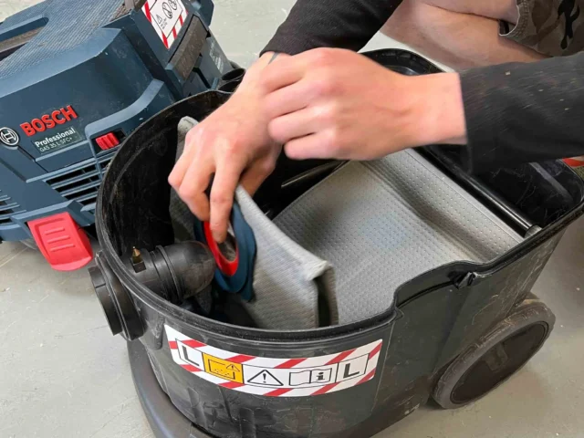 Macam reusable dust bag installed in Bosch VAC090 9-gallon dust extractor, showing gray three-layer polyester fleece material inside black collection basket