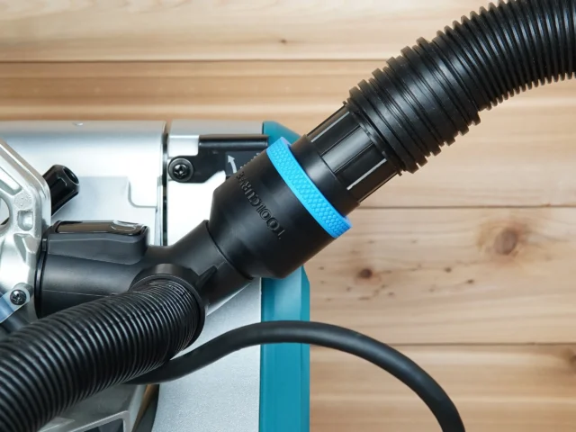 Black ToolCurve 1-7/8 inch hose adapter with blue ring joining a vacuum hose to a Makita miter saw port