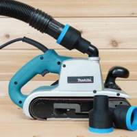 Black ToolCurve 1-7/8 inch hose adapter with blue ring joining a vacuum hose to a Makita 9403 belt sander, spare adapters beside it