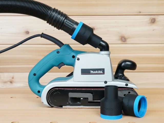 Black ToolCurve 1-7/8 inch hose adapter with blue ring joining a vacuum hose to a Makita 9403 belt sander, spare adapters beside it