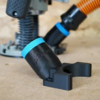 Black 1-1/4 inch hose adapter with blue collar and forked mount, standing on MDF beside a Bosch 1617 router