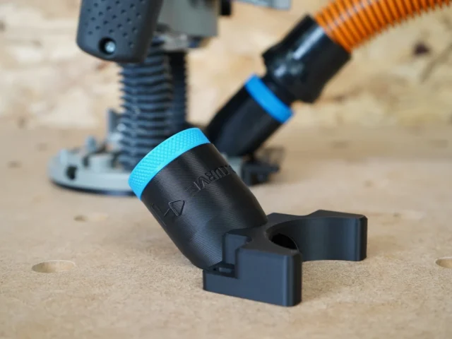 Black 1-1/4 inch hose adapter with blue collar and forked mount, standing on MDF beside a Bosch 1617 router