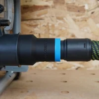 Black 27mm hose adapter with blue ring joining a green-striped vacuum hose to a SKIL table saw dust port