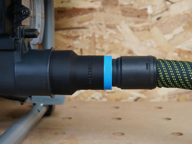 Black 27mm hose adapter with blue ring joining a green-striped vacuum hose to a SKIL table saw dust port