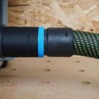Black ToolCurve 36mm hose adapter with blue ring joining a green-flecked hose to a SKIL table saw dust port