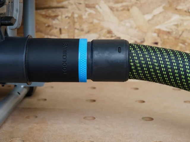 Black ToolCurve 36mm hose adapter with blue ring joining a green-flecked hose to a SKIL table saw dust port
