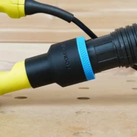 Black ToolCurve 1-7/8 inch hose adapter with blue ring joining a ribbed vacuum hose to a yellow Ryobi sander