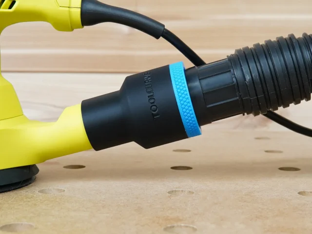 Black ToolCurve 1-7/8 inch hose adapter with blue ring joining a ribbed vacuum hose to a yellow Ryobi sander