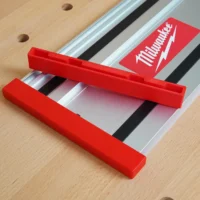 Red protective caps on both ends of a Milwaukee track saw rail, mounted on pegboard with product packaging visible above