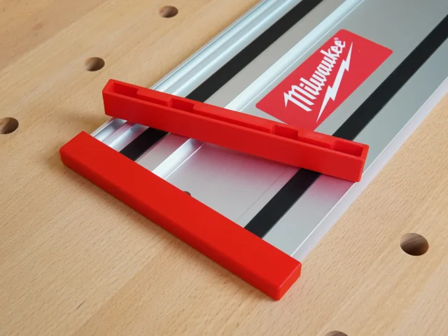 Red protective caps on both ends of a Milwaukee track saw rail, mounted on pegboard with product packaging visible above