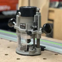 Porter Cable 6931 plunge router base riding a green-striped guide rail on an MDF benchtop via a black rail adapter