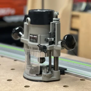 Porter Cable 6931 plunge router base riding a green-striped guide rail on an MDF benchtop via a black rail adapter