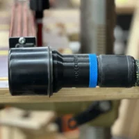 Hose adapter for Woodpeckers DP-PRO fence attached to drill press dust port, showing cylindrical black plastic connector with blue band and braided hose