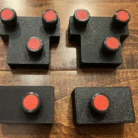 Two dark gray 3D-printed rail brackets with three and one red knurled knobs each, plus two smaller adapter blocks with single knobs