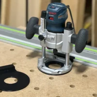 Black adapter plate disconnected from Bosch plunge router mounted on FS guide rail with dust collection hose