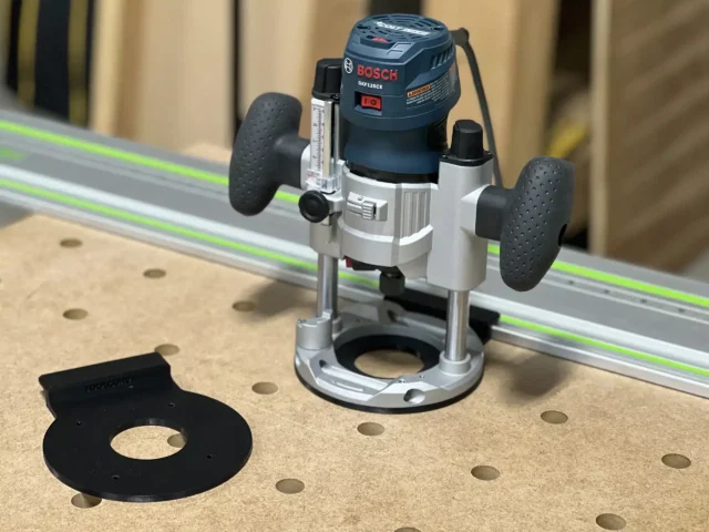 Black adapter plate disconnected from Bosch plunge router mounted on FS guide rail with dust collection hose