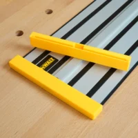 Two yellow protective caps on a DeWalt track saw rail, shown on wooden surface with mounting holes