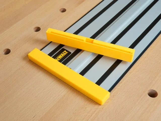 Two yellow protective caps on a DeWalt track saw rail, shown on wooden surface with mounting holes