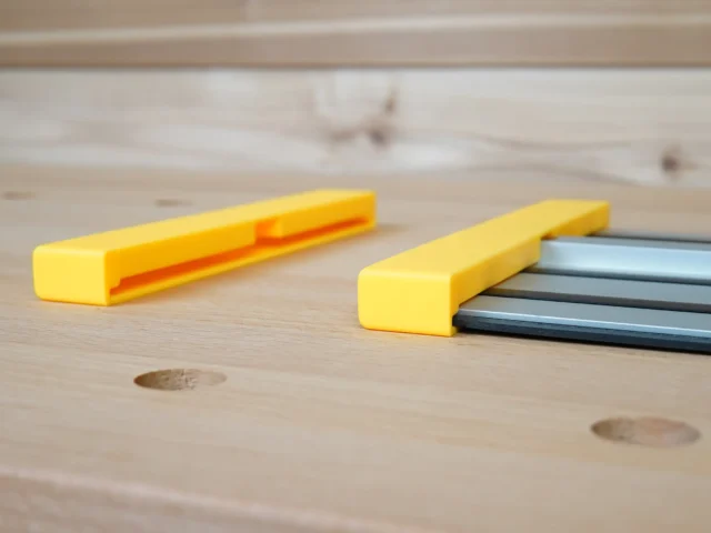 Two yellow Dewalt guide rail protective caps on wood surface; one shows interior channel detail, the other seated on dark aluminum track saw rail