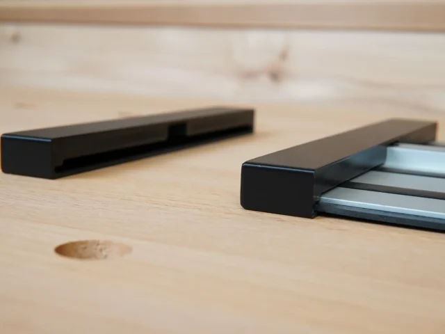 Two black Dewalt guide rail protective caps on a wooden surface, one shown alone and one slid onto an aluminum rail.