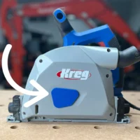 Blue arbor dust cover installed on the side of a grey Kreg ACS track saw, marked by a white arrow