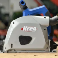 White dust cover with black foam seal attached to Kreg ACS track saw, showing snap-on design and low-profile housing over the blade arbor