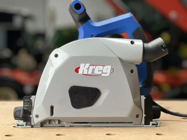 White dust cover with black foam seal attached to Kreg ACS track saw, showing snap-on design and low-profile housing over the blade arbor
