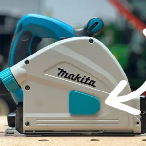 Makita SP6000J track saw side view with white arrow pointing to the installed teal arbor dust cover