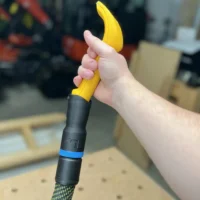 Yellow Proscrapper blade attached to black hose adapter with blue band, held in hand over workbench