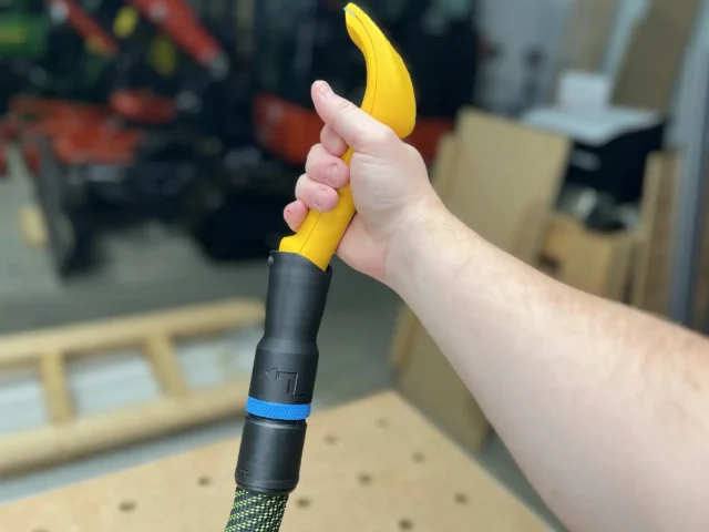 Yellow Proscrapper blade attached to black hose adapter with blue band, held in hand over workbench