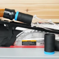 Black 1-1/4 inch hose adapter with blue band joining an orange hose to a SawStop jobsite blade guard port, spare adapters beside it