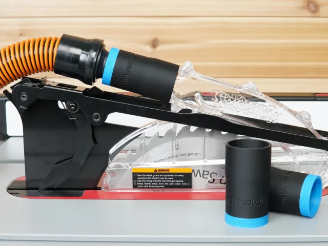 Black 1-1/4 inch hose adapter with blue band joining an orange hose to a SawStop jobsite blade guard port, spare adapters beside it