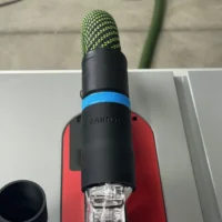 Black hose adapter with blue band attached to SawStop Jobsite table saw blade guard, showing green hose above and clear dust port below