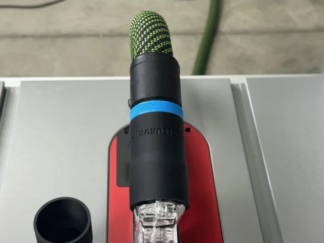 Black hose adapter with blue band attached to SawStop Jobsite table saw blade guard, showing green hose above and clear dust port below