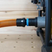 Black ToolCurve 1-1/4 inch hose adapter with blue band linking an orange vac hose to a DeWalt table saw dust port