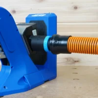 Black 1-1/4 inch hose adapter joining an orange vacuum hose to the dust port of a blue Kreg 720 pocket-hole jig