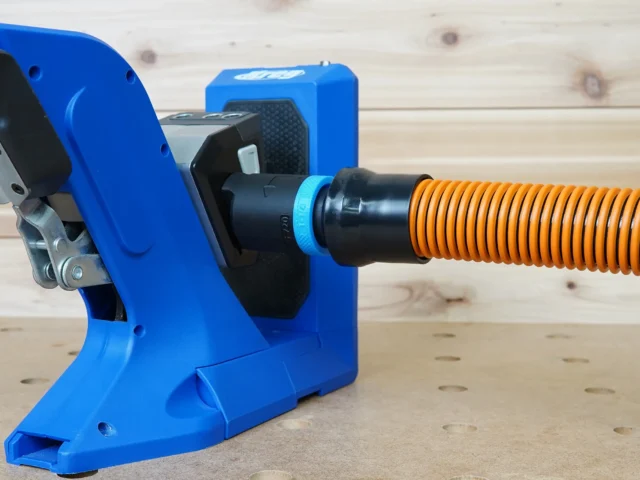 Black 1-1/4 inch hose adapter joining an orange vacuum hose to the dust port of a blue Kreg 720 pocket-hole jig