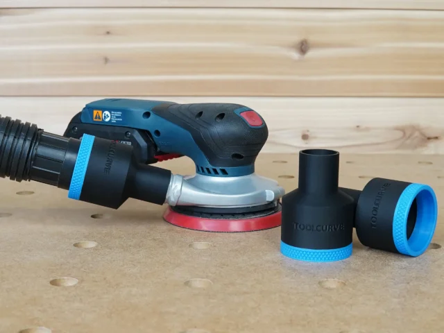Black and blue ToolCurve 1-7/8 inch hose adapter fitted to a Bosch GEX sander, with two spare adapters beside it